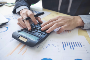 Hands on calculator on desk surrounded by work papers.